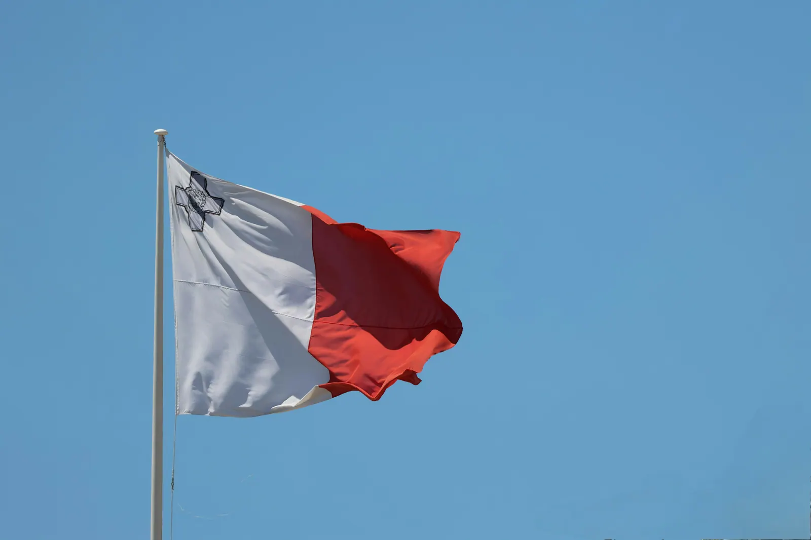 The flag of malta waves against a clear blue sky.