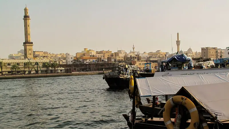 Hölzerne Abra-Fährboote am Dubai Creek, dahinter das Minarett der Großen Moschee und die niedrigen sandfarbenen Häuser des alten Bur Dubai.