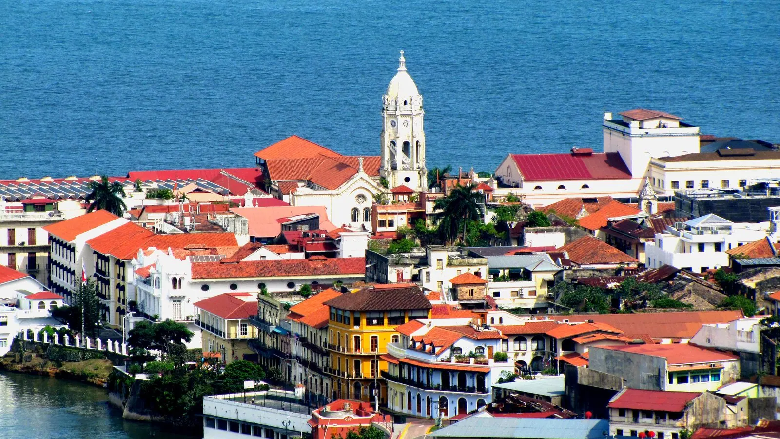 Die Altstadt von Panama-Stadt von oben: rote Ziegeldächer, Kolonialhäuser und der weiße Glockenturm einer Kirche vor dem blauen Pazifik.