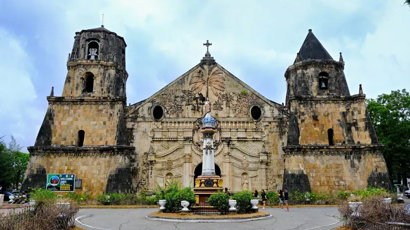 Die barocke Steinfassade und die zwei festungsartigen Glockentürme der Kirche von Miagao in Iloilo, Philippinen, unter bewölktem Himmel.