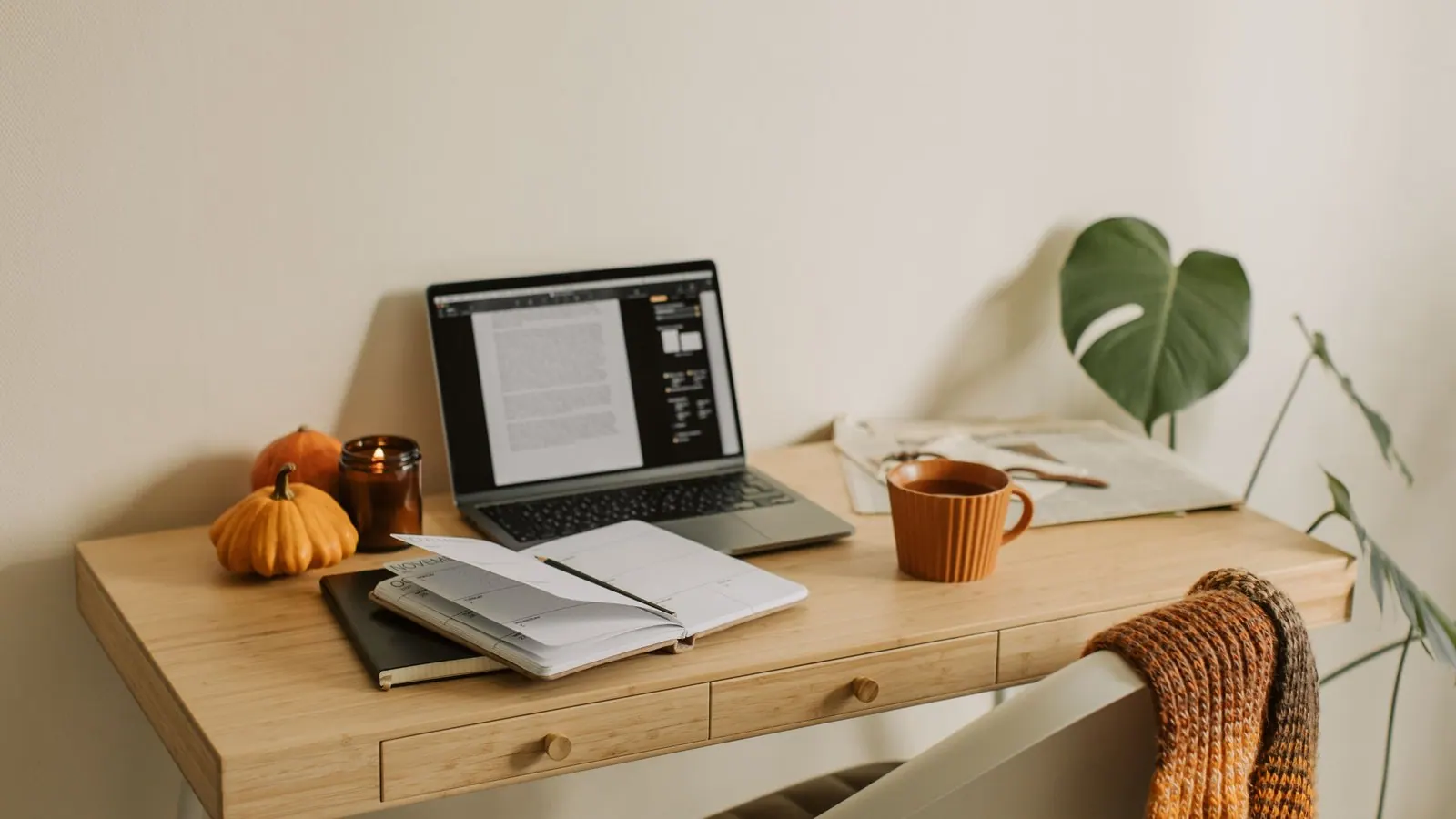 A bright home desk in autumn with a laptop, an open planner, a mug and a newspaper, the setting for filing a tax return before 31 October.